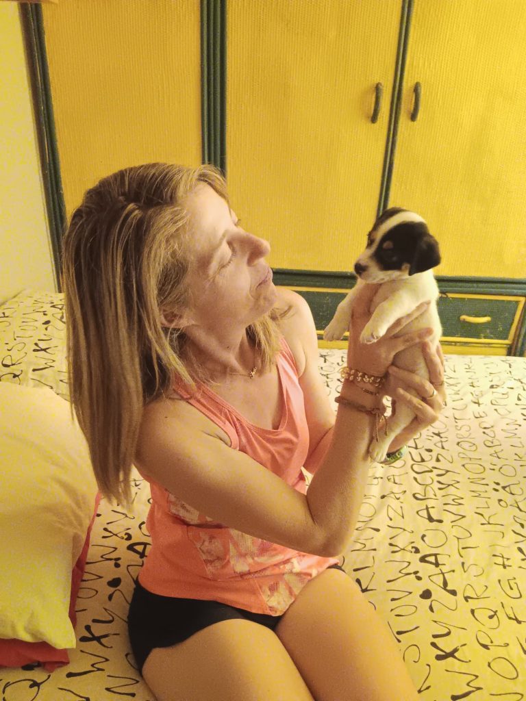 Mujer sentada sostiene a un perro pequeño en un espacio interior.